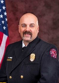 Formal photo of a chief officer sitting next to a flag in the background